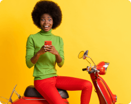 Mulher em pé, sentada em uma moto e olhando o celular